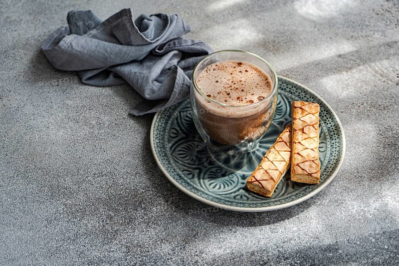 A delectable puff pastry filled with apricot jam is paired wonderfully with a steaming cup of freshly brewed cocoa, presented elegantly on a patterned blue plate beside a soft gray napkin