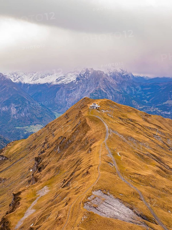 A path winds over a brown mountain ridge with snow-capped peaks in the background, Alpen Tower, Switzerland