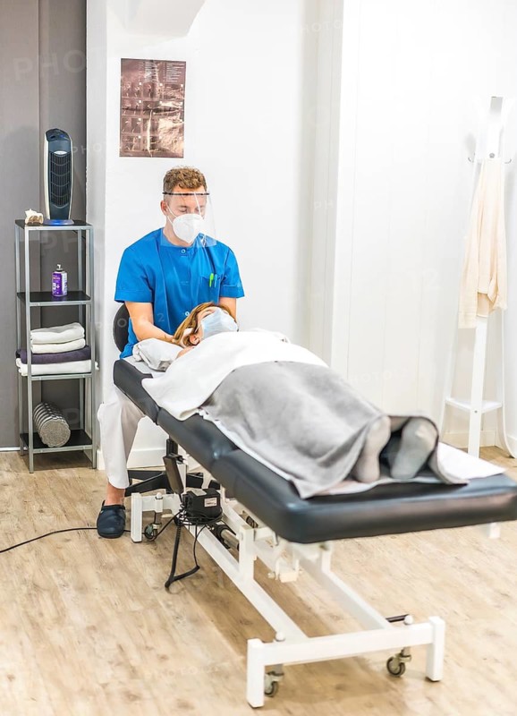 Physiotherapist with protective measures working with a patient on the stretcher, cranial osteopathy. Covid-19 pandemic. Osteopathy, therapeutic chiromassage