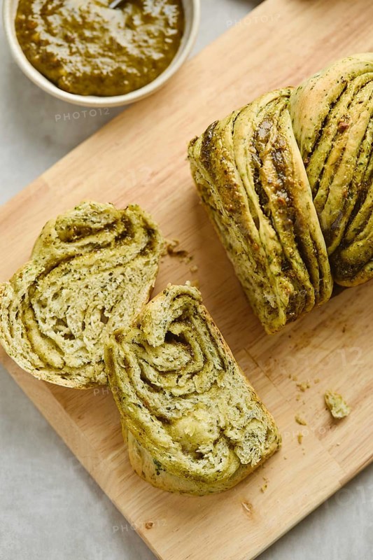 Baked homemade savoury babka plaited bread loaf flavoured with pesto on wooden bread board