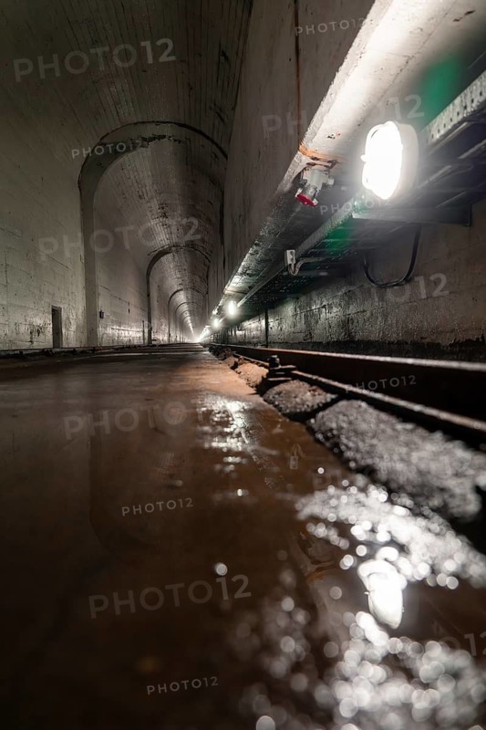Long concrete tunnel with damp floor and artificial lighting from the side, Rappbode Dam, Harz Mountains, Germany