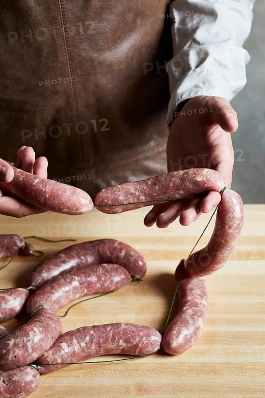 Butcher carefully handles fresh sausages, preparing them on a wooden surface. The image showcases the craftsmanship involved in traditional meat processing