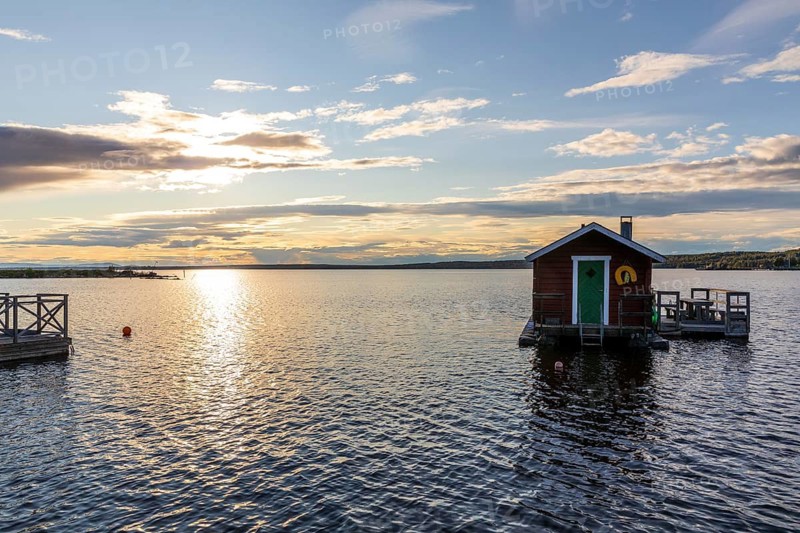 Small wooden house with seat on the water with boat dock, evening mood with sun and clouds on Lake Siljan in the port of Rättvik, Dalarnas län, Sweden