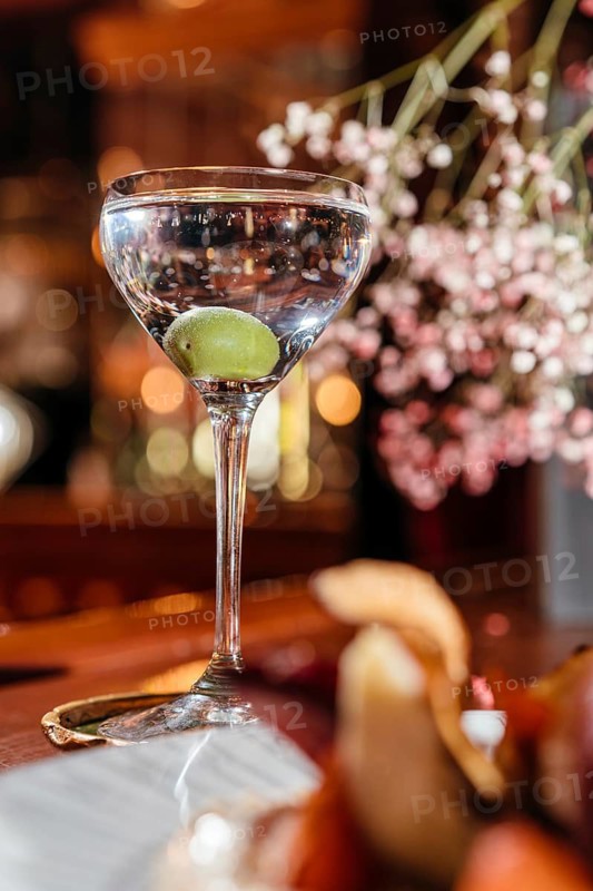 A classic dry martini garnished with an olive, elegantly presented in a crystal glass on a wooden bar. Perfect for sophisticated cocktail compositions
