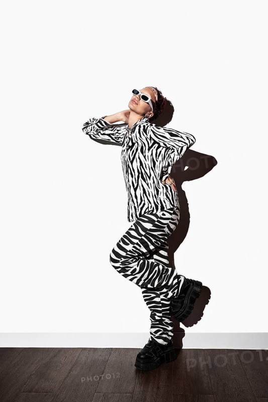 A model poses confidently in a striking zebra animal print ensemble. Wearing stylish sunglasses, the flash photography accentuates the design against a studio backdrop
