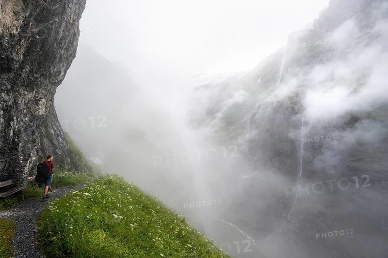 Mountaineer hiking on a hiking trail on a steep rock face, hiking to Berghaus Bäregg, cloud-covered rock gorge with waterfall, Bernese Alps, Bernese Oberland, Switzerland