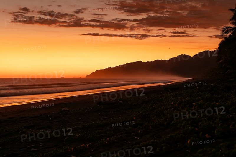 After sunset, the deep red sky glows above palms and ocean spray with views of Corcovado National Park. Costa Rica