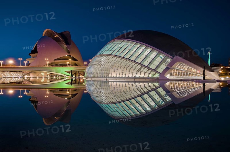 An evening view of the iconic City of Arts and Sciences in Valencia, Spain, showcasing the futuristic architecture beautifully reflected in the tranquil water under the blue sky