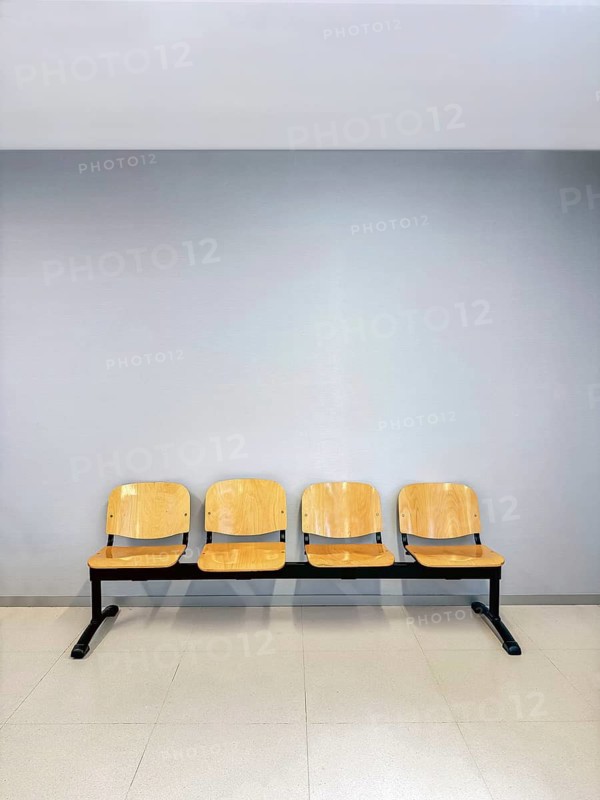 A row of four wooden chairs with metal frames placed against a light gray wall. The minimalist design and neutral colors lend a sense of calm and simplicity