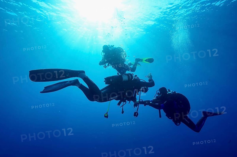 Three divers together underwater at a decorative stop, surrounded by sun rays and blue water, Giens Peninsula dive site, Mediterranean, Porquerolles, Provence, Côte d'Azur, France