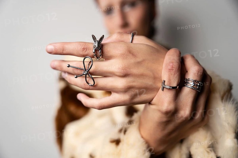 A close-up image of hands adorned with various stylish silver rings, showing intricate designs and elegance. The background is softly blurred, highlighting the rings