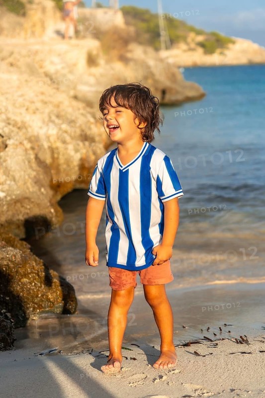 A young boy is standing on the beach with his arms outstretched, smiling. Concept of happiness and joy, as the child appears to be enjoying his time at the beach