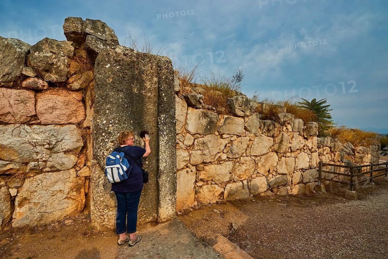 Cyclopean wall, gate, person leaning against an old stone wall with a view of a historic ruined site, Tiryns, ancient city in Argolis, Mycenaean, Peloponnese, Greece
