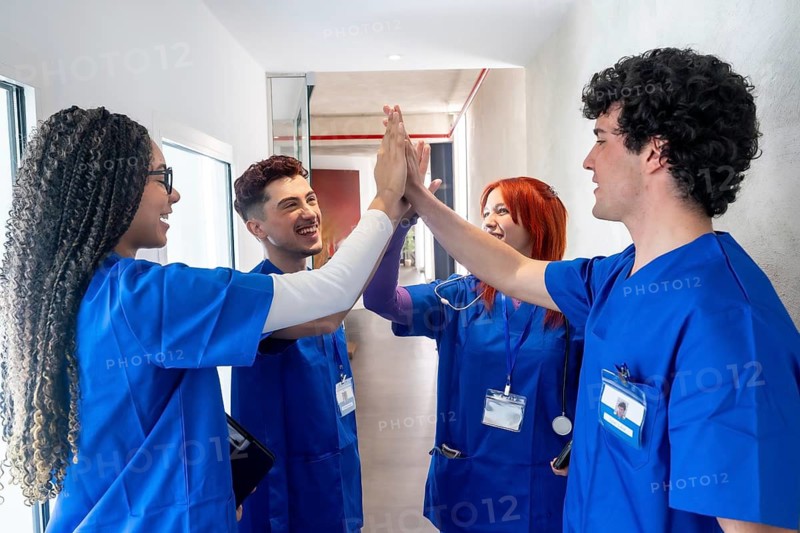 Medical students or young healthcare professionals celebrating success and demonstrating team spirit by high fiving in a modern hospital hallway after achieving a goal