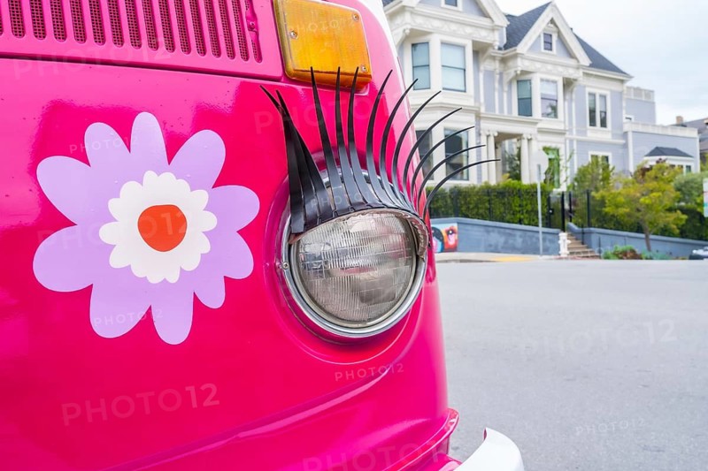 Pink custom van with decorative eyelashes and flower decal parked on a san francisco street, retro hippie vibe against classic victorian architecture, fun and nostalgic energy