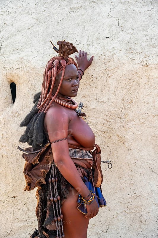 Married Himba woman leaning against a traditional mud hut, in the morning, traditional Himba village, Kaokoveld, Kunene, Namibia
