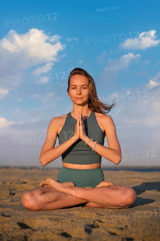 Woman in padmasana lotus pose on sandy beach at sunset, hands in namaste, embodying tranquility and mindfulness in nature