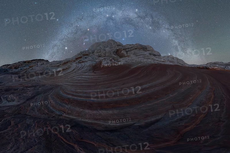 Stellar Milky Way galaxy arching above the swirling, layered rock formations of a Utah desert landscape under a dark, starry sky