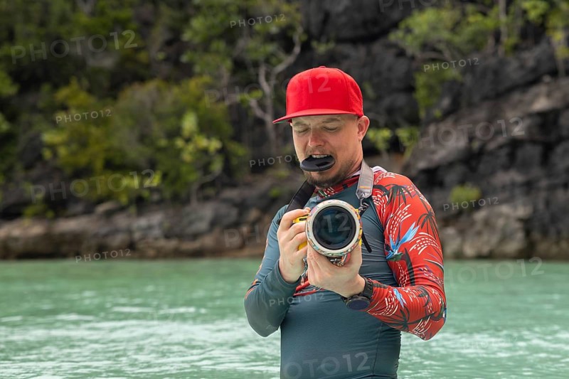 A photographer in a red cap takes pictures in Raja Ampat, Indonesia Turquoise water and lush greenery complement the vibrant scene, capturing the spirit of adventure and nature