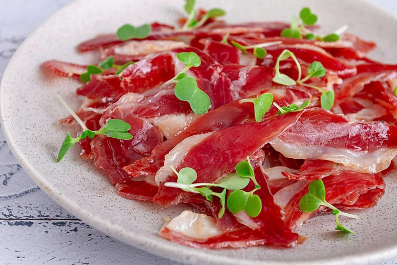 Ham of duck breast, dried duck fillet, with microgreens, plate, on a tiled table