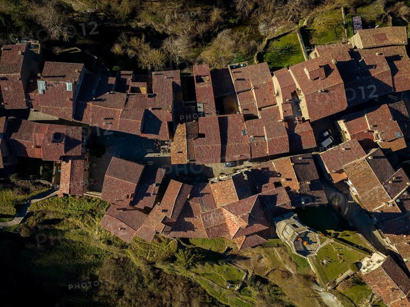Aerial image of a charming historic village with traditional terracotta rooftops in Montserrat, Catalonia, Spain. The intricate layout is surrounded by lush greenery