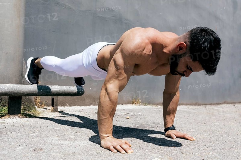 Athletic man demonstrating strength and fitness by performing a push-up outdoors on concrete, highlighting his toned physique and commitment to a healthy lifestyle