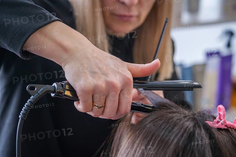 A hair stylist is using a flat iron to straighten hair in a beauty salon. The stylist focuses on achieving smooth, straight hair for the client. This treatment enhances the hair's appearance