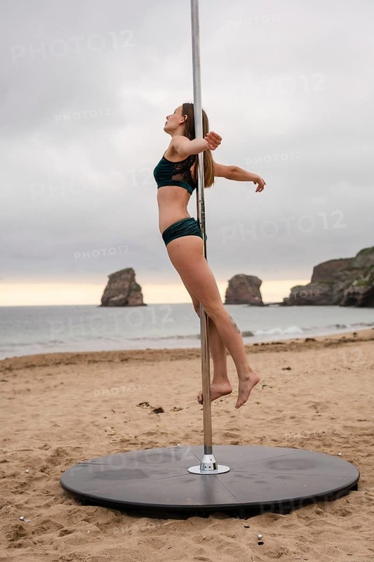 Young caucasian girl performing pole dance at a beautiful beach. Acrobat performing a pole dance in the sand of the beach of Hendaya, France
