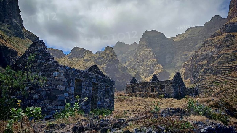 Stone ruins of old houses made of volcanic stone against a spectacular mountain backdrop with thick clouds, hiking, lost place, abandoned village of Formiguinhas, Marinha da Cruzinha Natural Park, Santo Antao, Cabo Verde, Cape Verde, Cape Verde