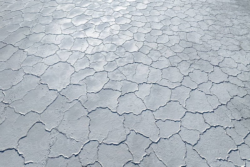 Aerial view of a saline mudflat with a distinctive cracked surface pattern. The image captures the desolate and natural beauty of dried mud, highlighting its unique texture