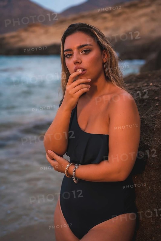 Lifestyle of a blonde Caucasian girl in a black swimsuit next to a rock in the sea