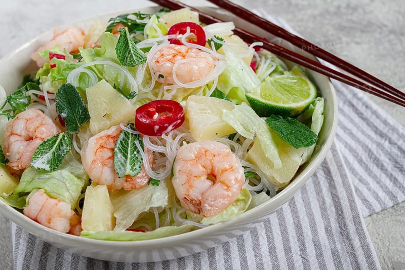 Thai salad with shrimp and rice noodles, pineapple slices, coriander and mint leaves, on a white plate, homemade, no people