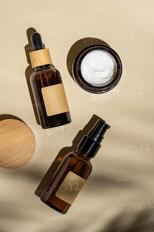 Top view of a sophisticated arrangement of cosmetic bottles with wooden caps and blank labels casting gentle shadows on a beige background, symbolizing eco-friendly beauty products