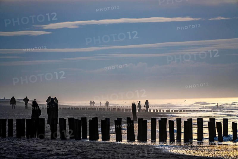 Winter on the North Sea, sunset at sea, beach walkers, coastal protection, through wooden posts, paalhoofden, on the beach, breakwater, the piles rammed into the sandy soil in double rows slow down the waves and ocean currents and thus slow down the flow rate of seawater, so less sand is washed away from the standing position, near Domburg, Walcheren peninsula in the Dutch province of Zeeland