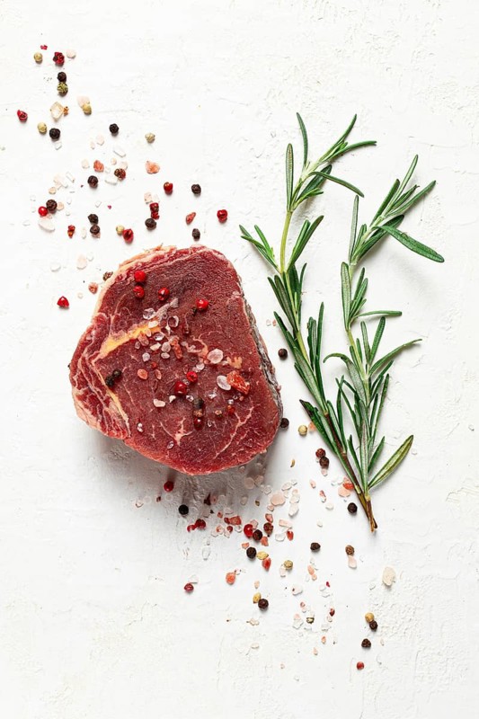 Fresh, raw rib eye steak, with spices, on a white background, top view