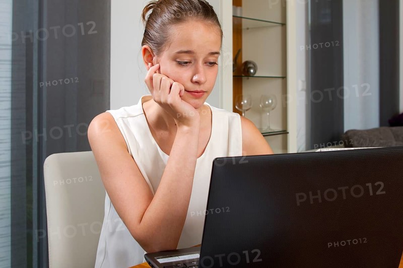 A young woman looks sceptically at her computer, at the laptop