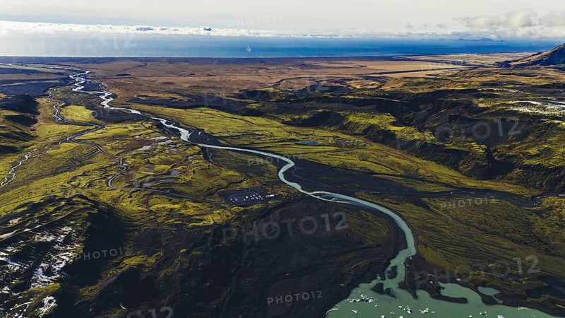 Wide aerial view of braided rivers flowing through mossy and volcanic terrain in southern Iceland, with meltwater from glaciers weaving across the vast floodplain toward the sea