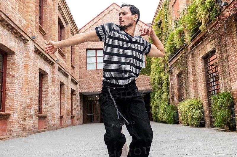 A Cuban man passionately dances in a vibrant urban courtyard, surrounded by brick buildings and greenery, showcasing dynamic movement and artistic expression