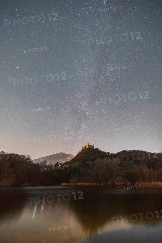 Captivating night view of Castello di Montalto, illuminated under a starry sky. The serene Lago Pistono reflects the castle and the distant, visible stars