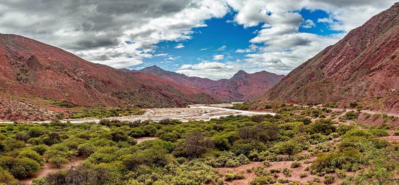 Panoramic view of red mountains and vegetation with clouds, the landscape and colorful rock formations of the Quebrada de Cafayate near Salta in Argentina