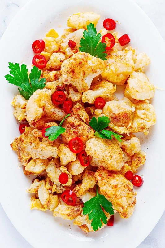 Cauliflower dish, with chili pepper and parsley, on a white plate served on a marble countertop