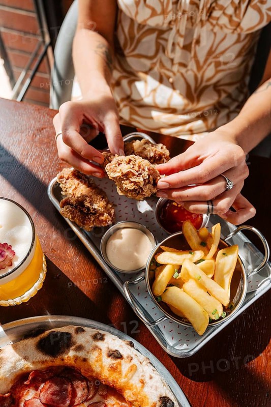 Chicken wings served with dips alongside crispy fries and a pizza. Accompanied by a refreshing cocktail, creating a delightful meal setting. Ideal for food enthusiasts