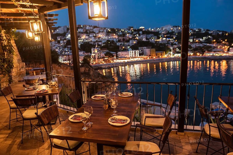 ULCINJ, MONTENEGRO - JUNE 22, 2019: Tables in restaurant with view on the city at night.