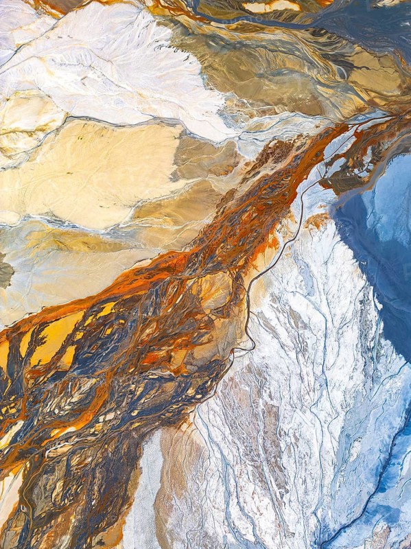 From above, an aerial drone image captures the intricate and abstract patterns of natural formations. The photograph showcases a blend of earthy tones and textures that resemble an artistic palette