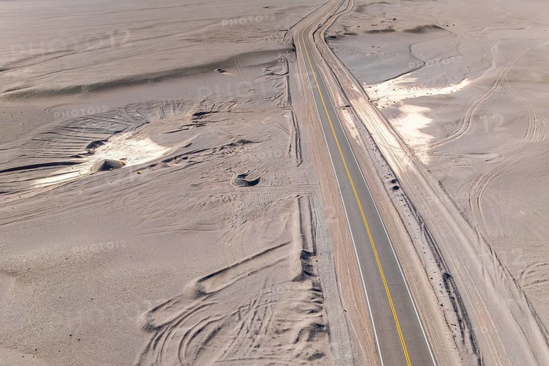 Aerial view of a long, solitary asphalt road cutting through an expansive desert landscape of the argentine Puna. The scene captures the vastness and isolation of the arid environment