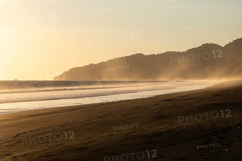 The low sun's golden light illuminates the ocean spray on Carate Beach, with views of Corcovado NP at sunset. Costa Rica
