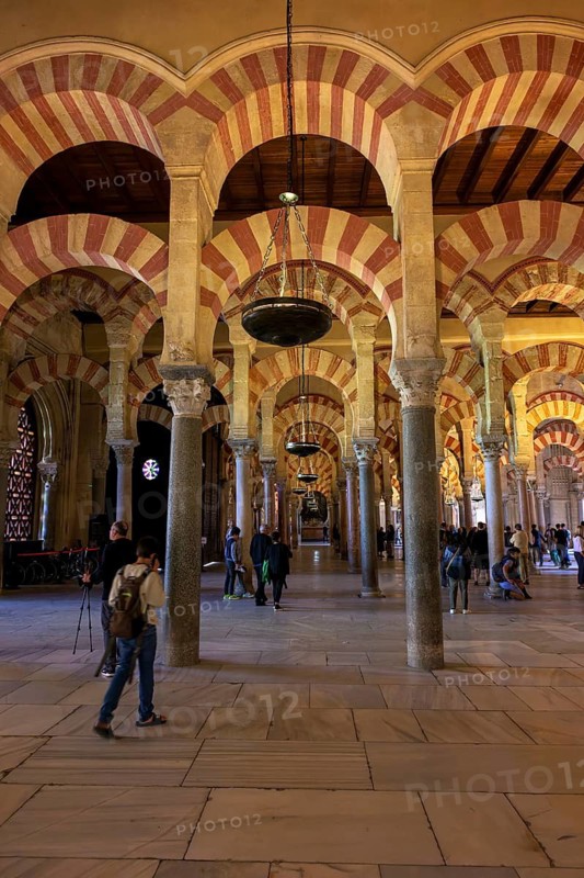 A long corridor with large arches and columns of the Cathedral Mosque of Córdoba (Mezquita-Catedral), filled with people admiring the architecture, Cordoba, Andalusia, Spain