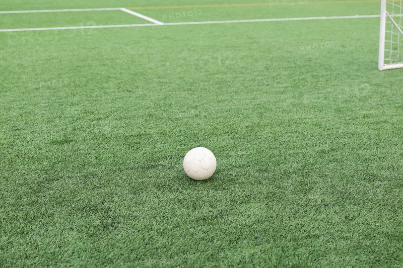 A close up shot of a soccer ball resting on a lush green field with a soccer goal in the background, capturing the essence of the game, textures and its environment