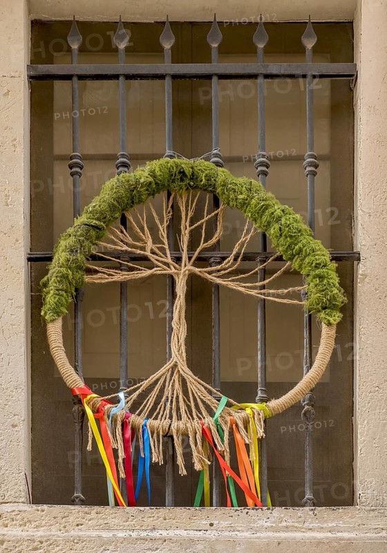 A peace wreath made of rope and moss with colourful ribbons hangs in front of a window grille