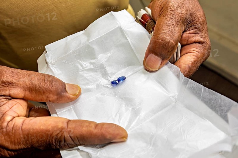 Two precious stones on white paper, held by hands. Focus on craftsmanship and detail, the sapphire emeralds and gemstones of the city of Ratnapura in Sri Lanka